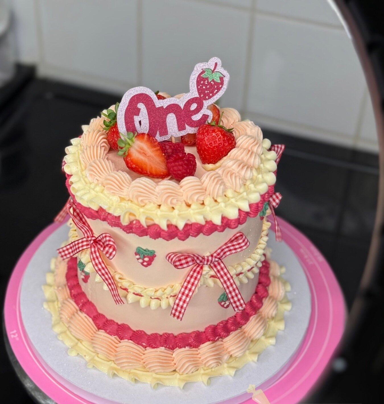 Pink buttercream first birthday cake topped with strawberries and a number one topper